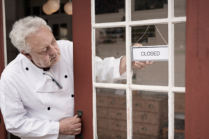 Older chef closing restaurant with 'Closed' sign on the door