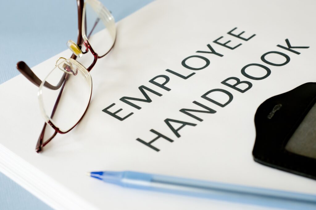 Close-up of an employee handbook with eyeglasses and a pen, symbolizing workplace policies, employee guidelines, and professional standards.